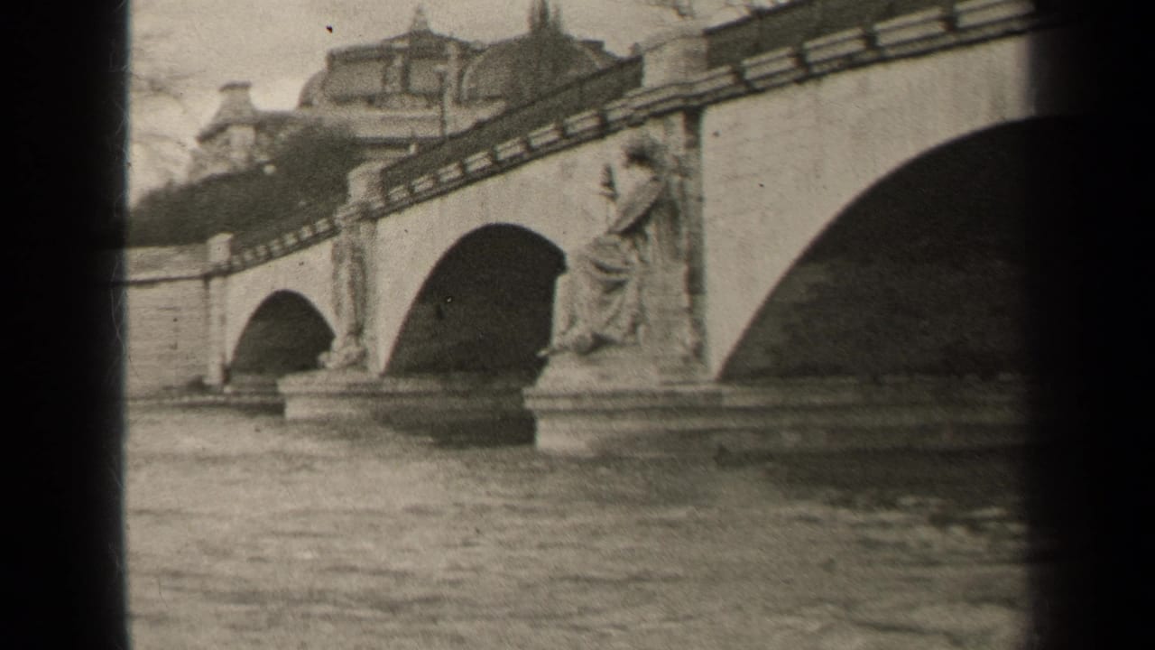 1947 Paris home-movie frame showing a stone arch bridge, river water, and a seated classical statue near the parapet.