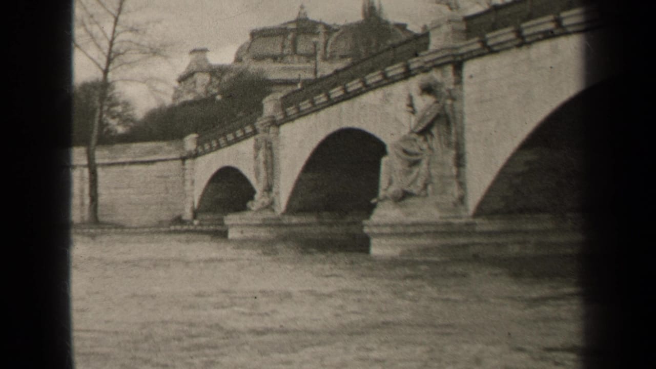 1947 Paris 8mm frame with bridge arches, a sculpted figure on a pedestal, bare trees, and a domed building beyond.