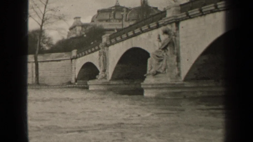 Paris 1947 home-movie frame showing the river, stone bridge arches, and a seated statue beside a large arch opening.