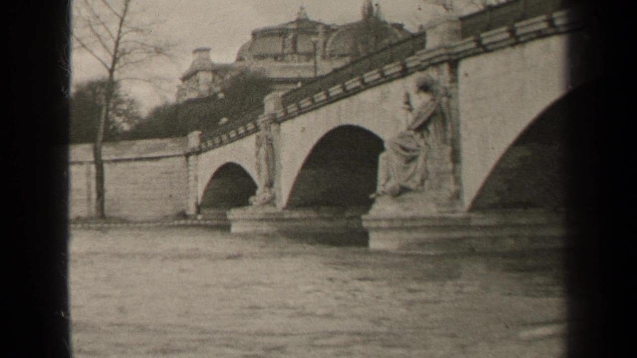 1947 Paris frame with a multi-arch stone bridge, a statue on the river pier, bare trees, and classical buildings beyond.