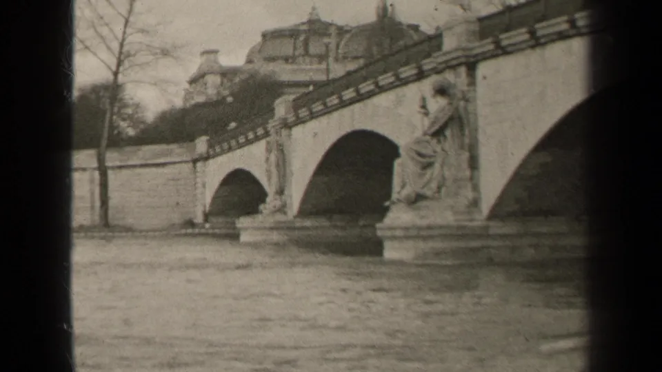 1947 Paris frame with a multi-arch stone bridge, a statue on the river pier, bare trees, and classical buildings beyond.