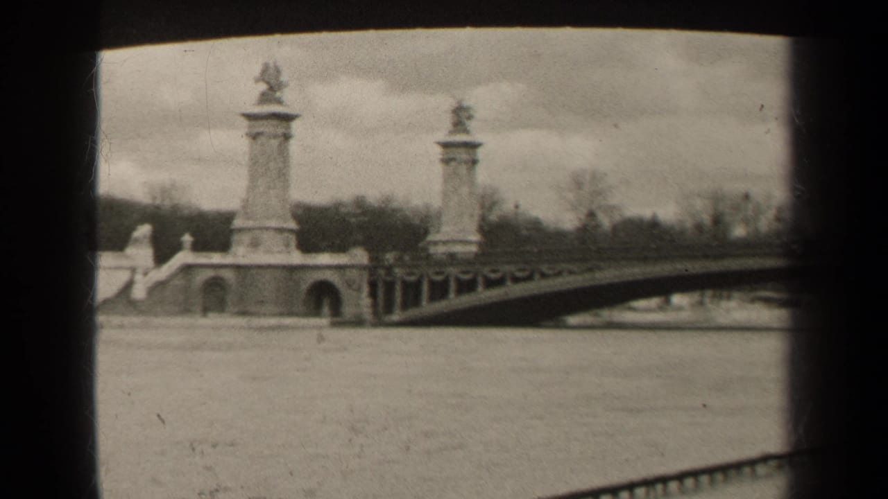 1947 Paris frame with the bridge entrance, two stone pylons, arched openings, railings, river surface, trees, and overcast sky.