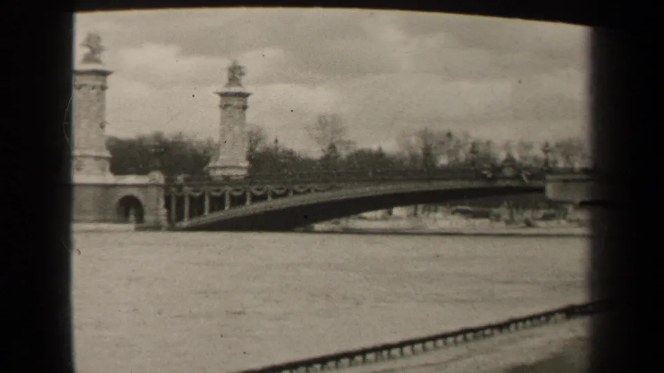 1947 Paris home-movie still showing the bridge railing extending over the river, with a stone pylon at left and trees beyond.