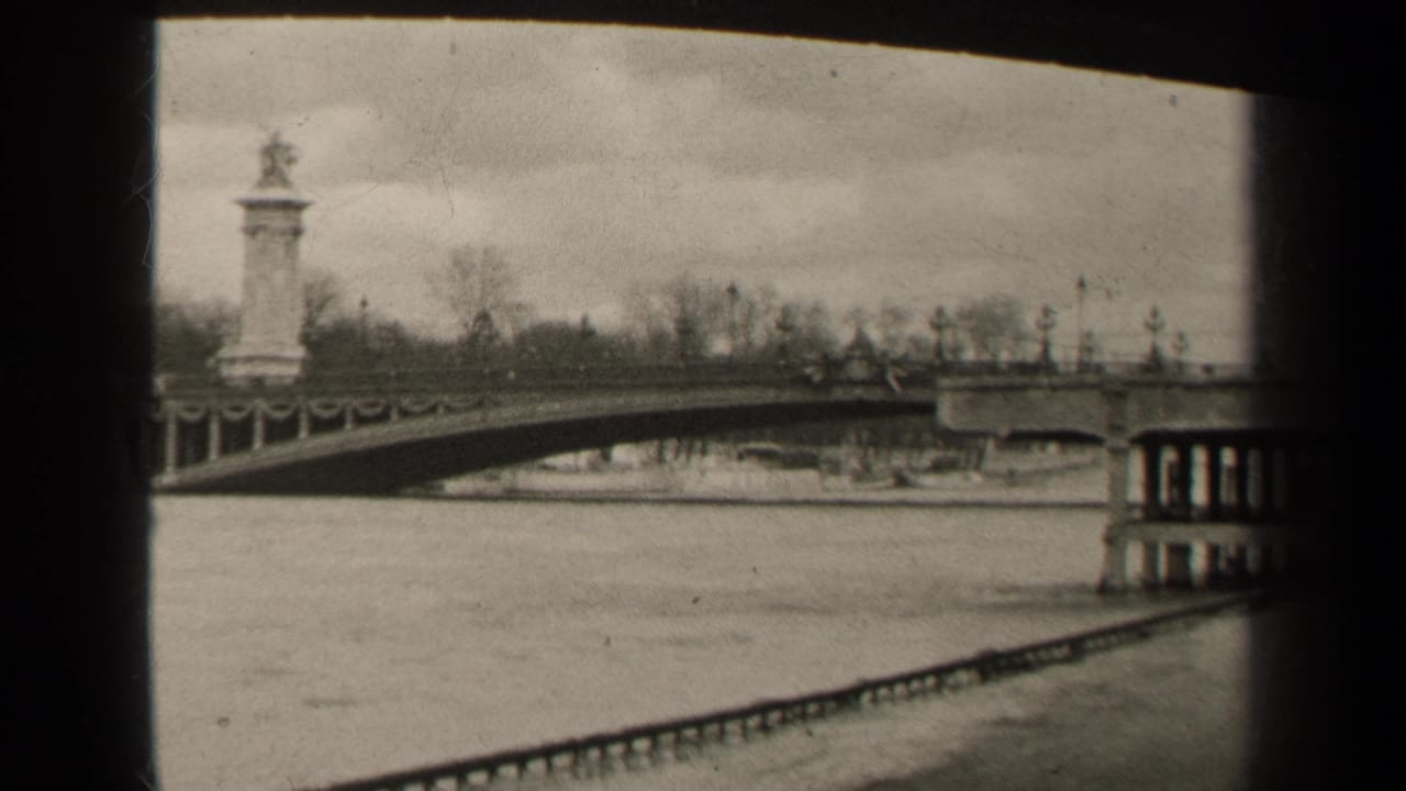 Black-and-white river view with an arched bridge, tower-like structure, and car on the span.