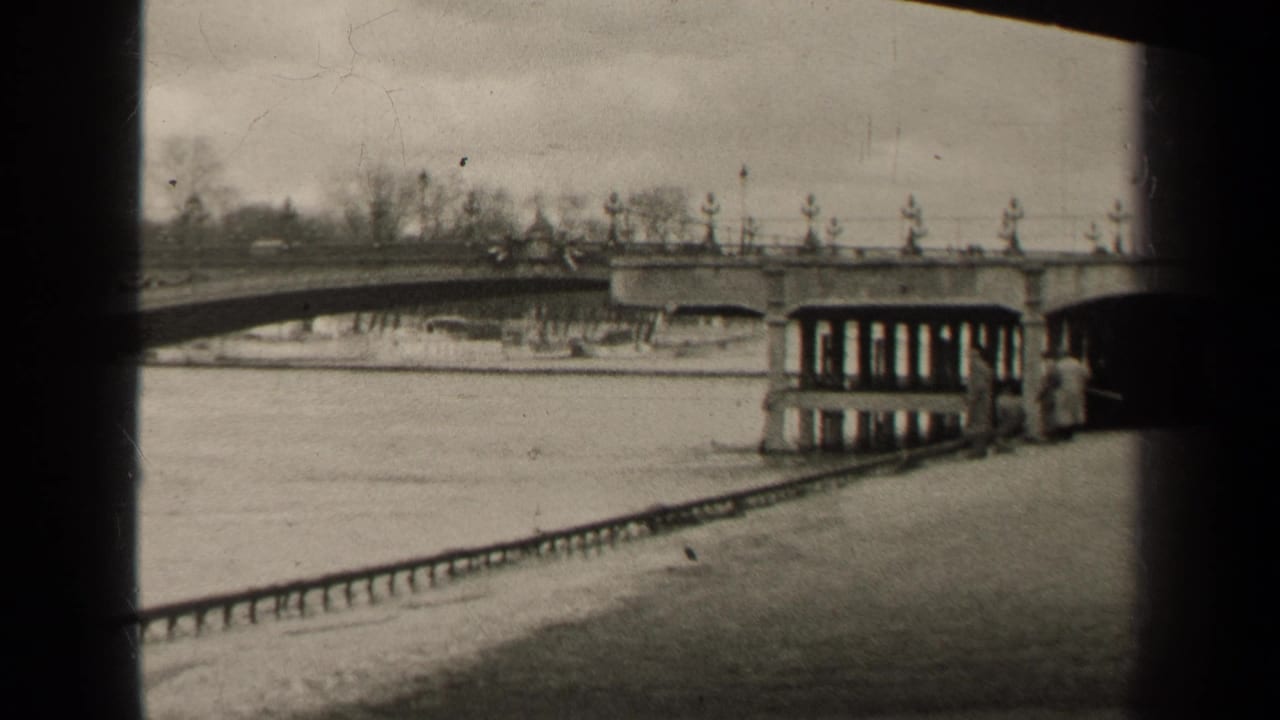 1947 Paris home-movie frame showing a stone bridge over the river, a small riverside structure, and dark edges from the film scan.