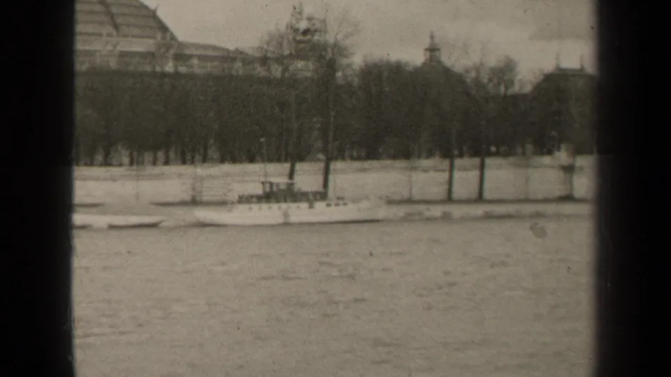 1947 Paris river view with a small boat, bare trees, stone embankment, and soft historic building silhouettes in the background.