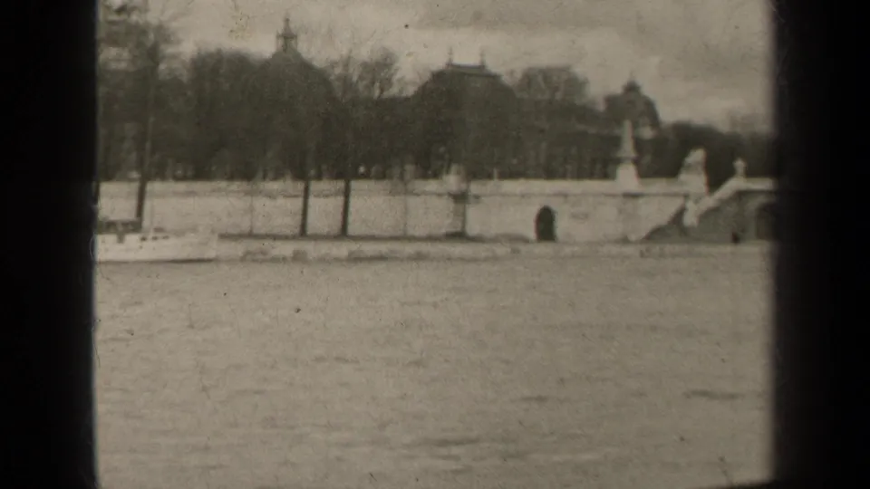1947 Paris river scene showing a stone bridge approach, embankment wall, trees, distant buildings, and a monument entering frame.