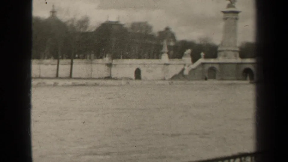 1947 Paris view across the river to a stone bridge with arched openings, a tall monument column, and a statue above the embankment.