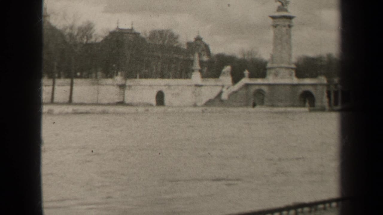 1947 Paris home-movie frame showing a broad river crossing with ornate bridge columns, stone arches, bare trees, and distant buildings.