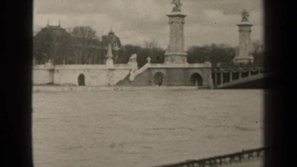 1947 Paris frame with a monumental bridge crossing the river, sculptural columns, arches, railing, bare trees, and distant architecture.
