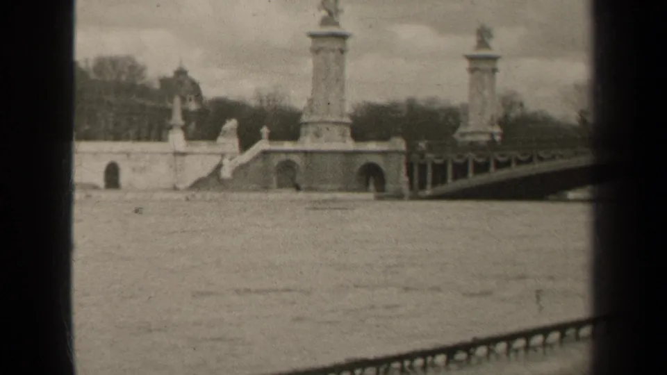 1947 Paris home-movie frame emphasizing the bridge columns, arched embankment openings, steps, railing, and river foreground.