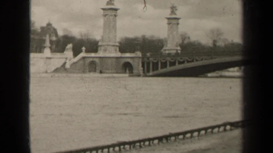 1947 Paris frame showing the river and ornate bridge structure, with columns, arches, railing, winter trees, and distant buildings.