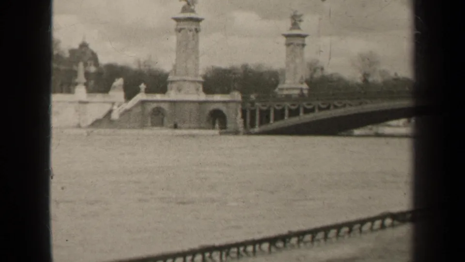 1947 Paris home-movie frame showing a river, distant stone bridge columns, balustrade, and overcast sky.