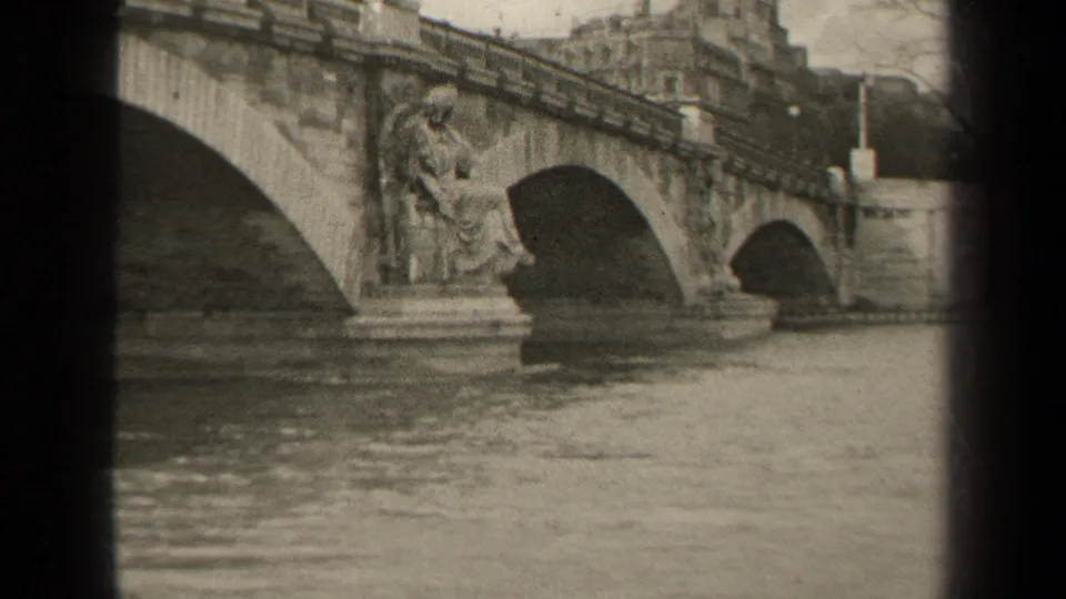 1947 Paris 8mm frame showing an ornate multi-arch stone bridge crossing calm river water.