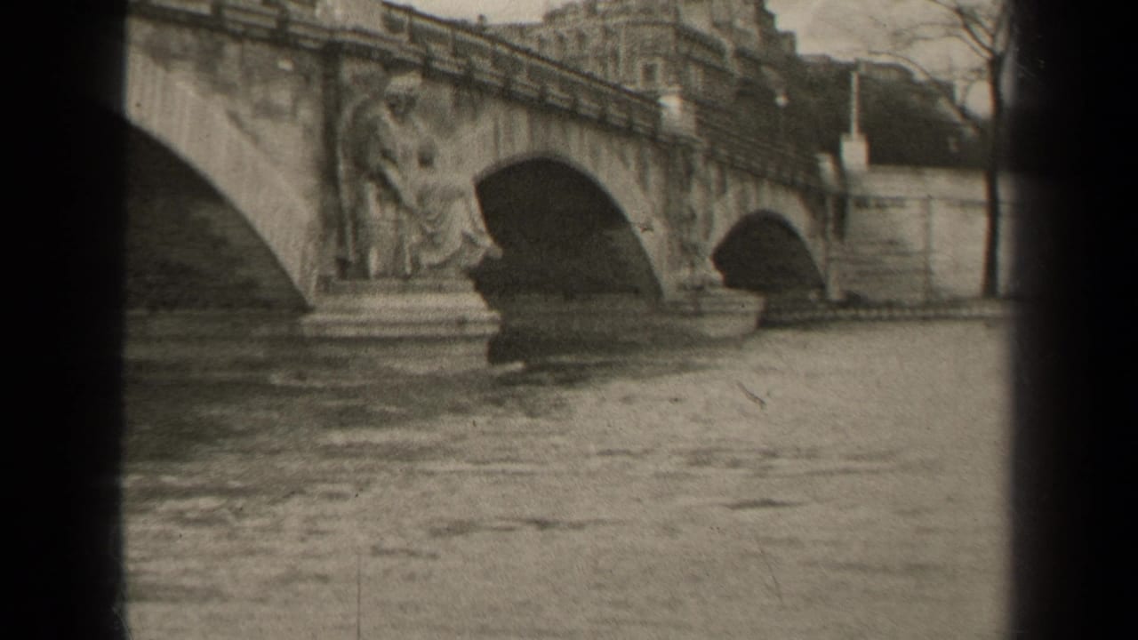 1947 Paris home-movie frame showing a stone bridge with arched spans, sculpted figures, river water, and buildings beyond.