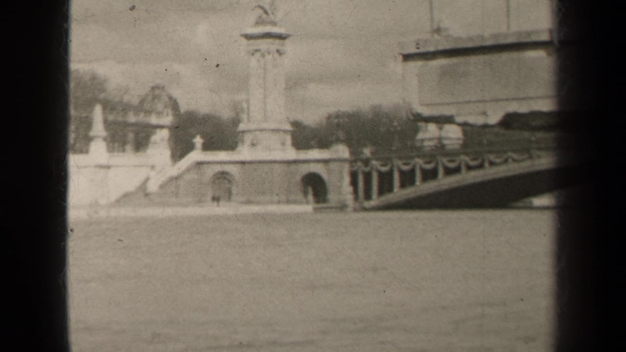 1947 Paris home-movie frame showing a tall stone monument, bridge railings, and riverside architecture in soft black-and-white 8mm.