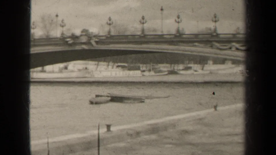 Paris 1947 home-movie frame showing an ornate bridge span with lampposts above the river and small boats visible below.