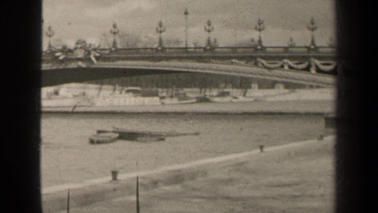 1947 Paris home-movie frame showing an ornate bridge railing, lamps, riverboats and paved embankment in black and white.