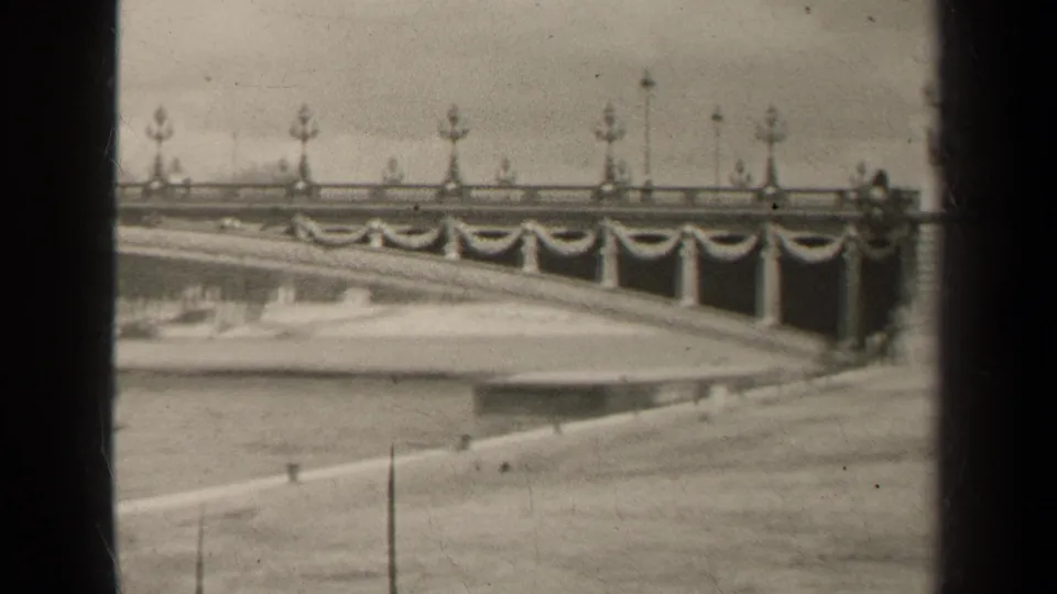 1947 Paris bridge detail in soft black-and-white 8mm, showing lamps, draped railings and the riverfront edge.
