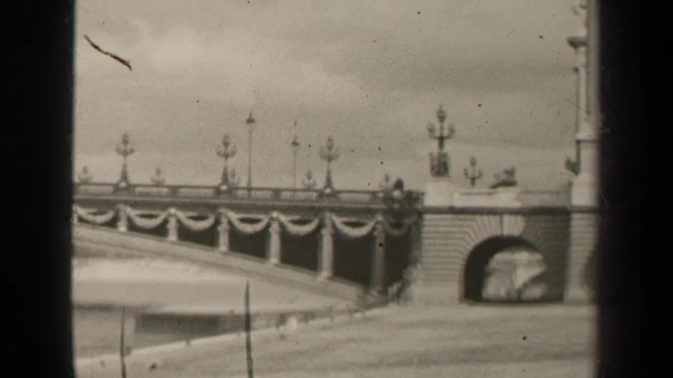 Black-and-white 1947 Paris frame showing the bridge end, an arched underpass, lamps and draped railing banners.