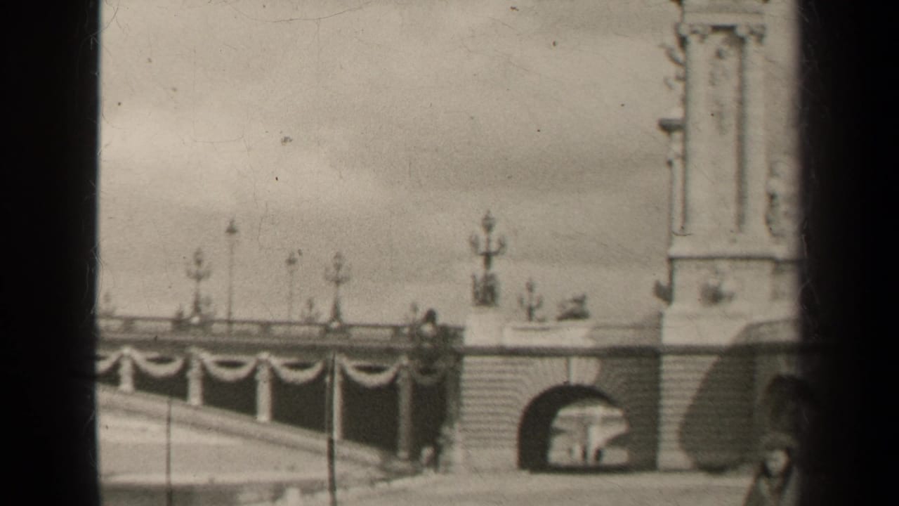 1947 Paris home-movie frame showing a stone bridge approach with arched opening, ornate lampposts, draped decoration, and part of a monument.