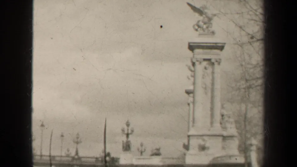 1947 Paris frame showing a tall sculptural pedestal topped by a winged horse, with ornate lampposts, bare branches, and cloudy sky.