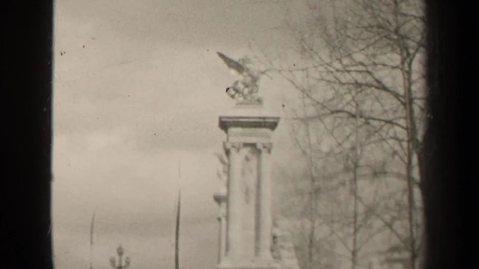 1947 Paris frame with the winged horse sculpture and tall stone pedestal set against bare branches, open sky, and visible 8mm frame edges.