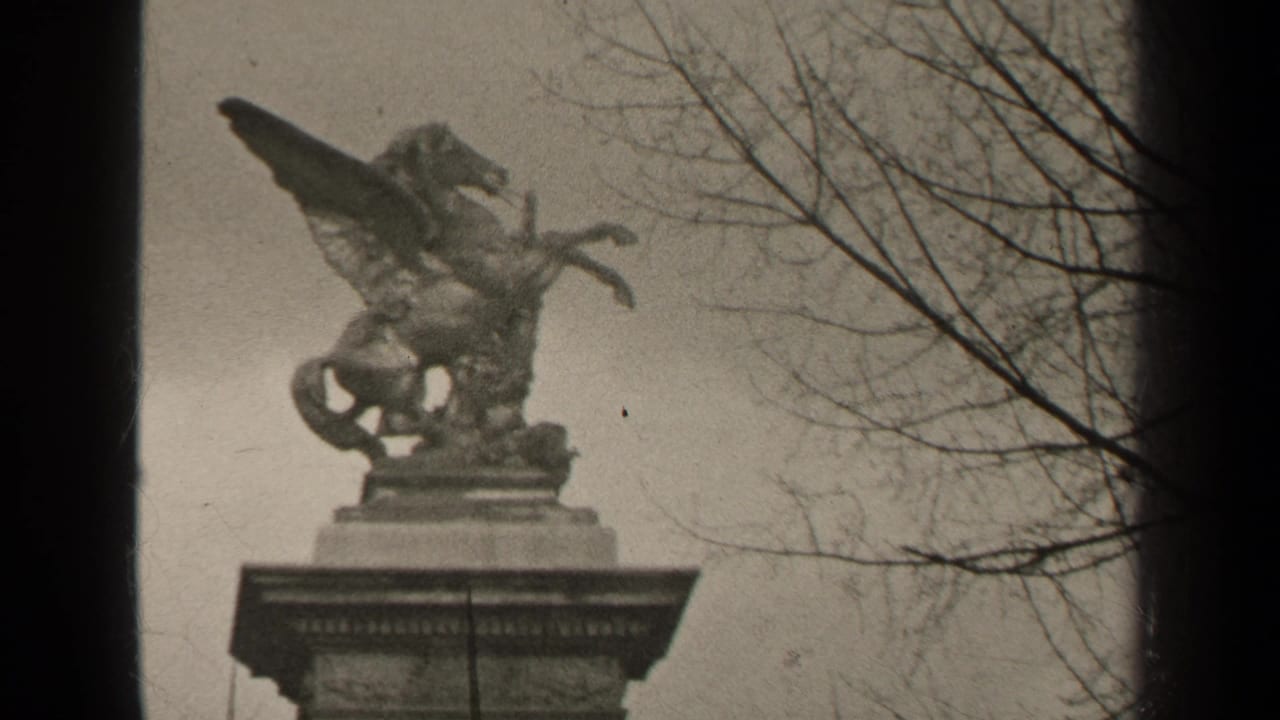 1947 Paris 8mm frame showing a Pegasus-like statue on a pedestal, filmed from below with bare tree branches at right.