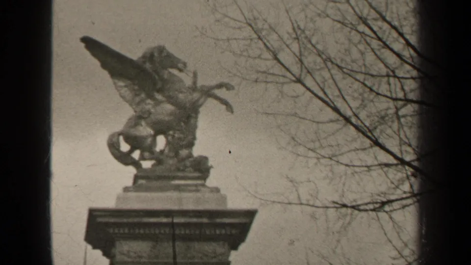 1947 Paris 8mm frame showing a Pegasus-like statue on a pedestal, filmed from below with bare tree branches at right.