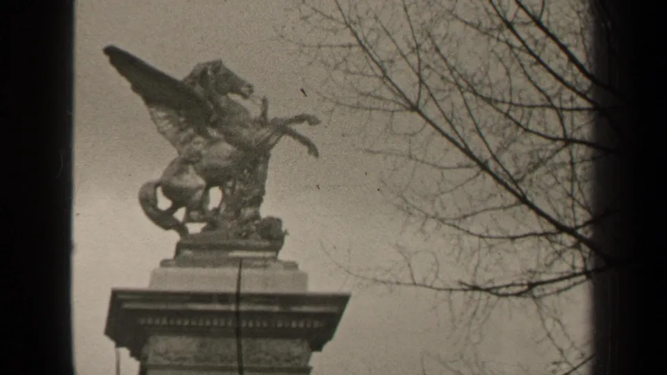 1947 Paris 8mm frame showing the winged horse statue from a low angle, with bare branches and visible film wear.