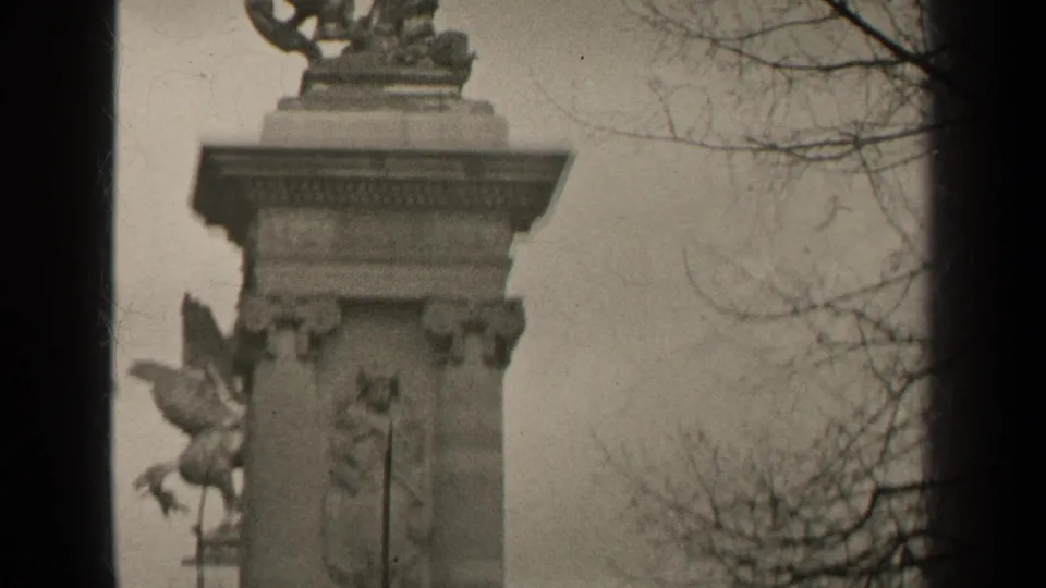 Paris 1947 home-movie frame with a tall decorated pier, partial winged horse sculpture, and leafless tree branches.