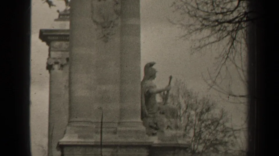 Paris home-movie frame from 1947 showing a monumental stone pier, seated sculpture, and winter tree branches.
