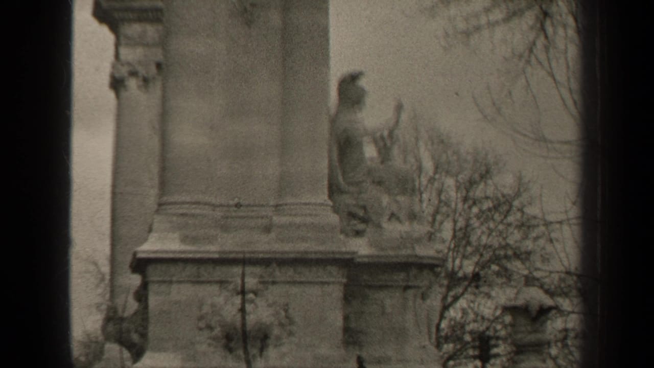 1947 Paris 8mm frame showing part of a stone monument with a seated figure, bare branches, and visible film borders.