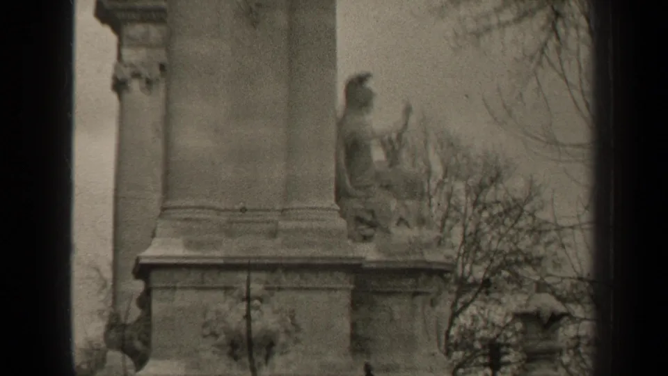 1947 Paris 8mm frame showing part of a stone monument with a seated figure, bare branches, and visible film borders.