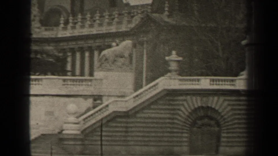 1947 Paris 8mm frame showing ornate stone steps, balustrades, an arched doorway, and a lion statue on a classical monument.