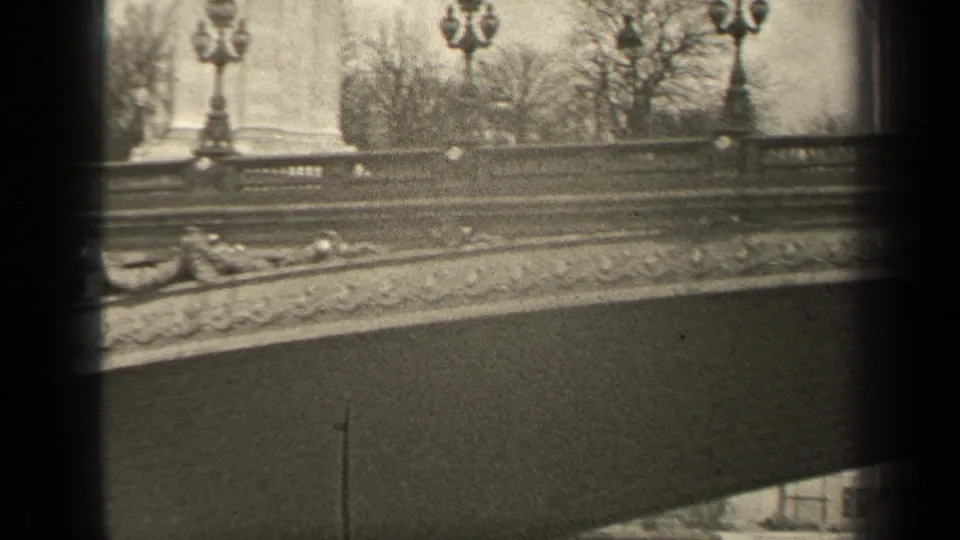 1947 Paris frame showing an ornate bridge railing, lampposts, bare trees, and small distant people on the walkway.