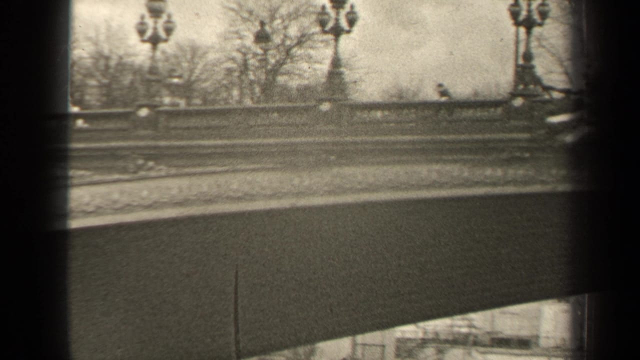 1947 Paris home-movie frame showing a decorated bridge balustrade, globe lampposts, bare trees, and passing-vehicle motion blur.