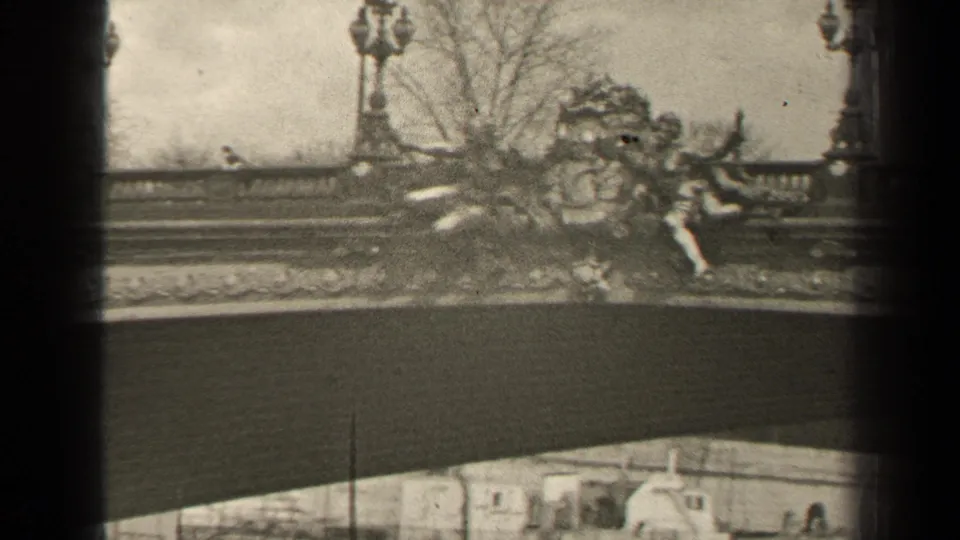 1947 Paris frame with ornate bridge sculpture, multi-globe lampposts, balustrade, and pale buildings glimpsed below the span.