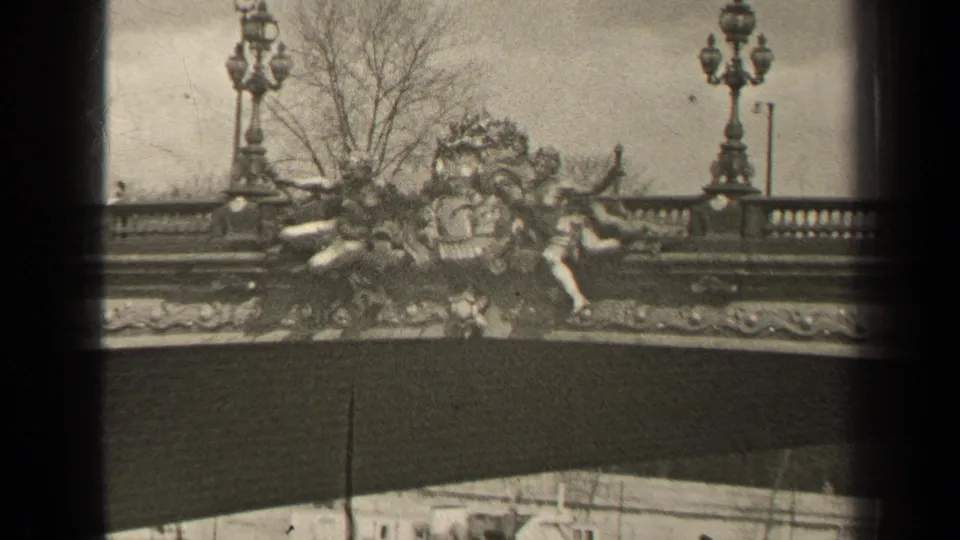 1947 Paris home-movie view of sculptural bridge decoration with a lamppost, leafless trees, and a distant pedestrian on the walkway.