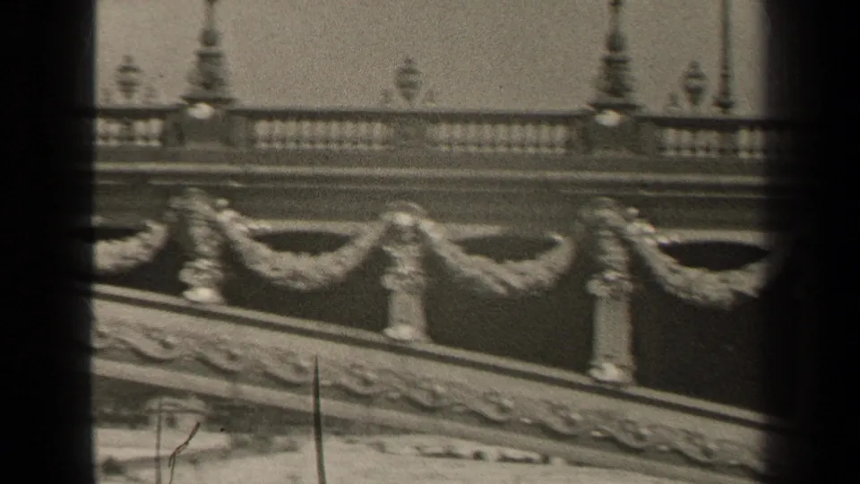 Final 1947 Paris bridge frame with sculpted garland details, balustrade, lampposts, and grainy home-movie softness.
