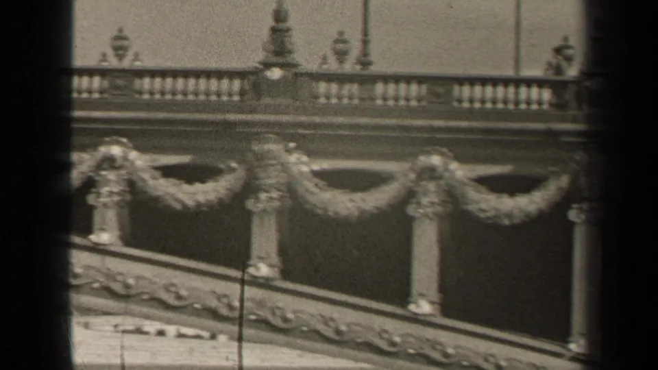 1947 Paris home-movie frame showing decorative stonework, balustrades, and garland-like ornament viewed through dark vertical foreground bars.