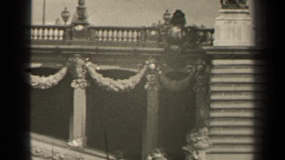1947 Paris frame with balustrade, sculptural ornament, steps, and small distant pedestrians near a decorative stone structure.