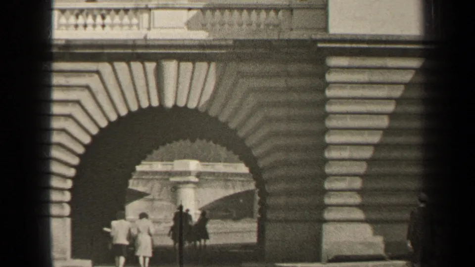 1947 Paris frame showing people beneath a broad stone arch, with balustrades and decorative masonry visible above.