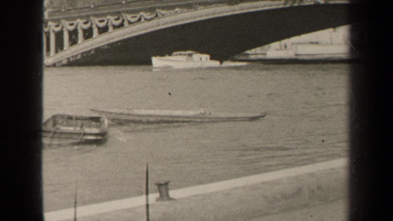 Boat moving on a river beneath an ornate arched bridge with quay edge in foreground.
