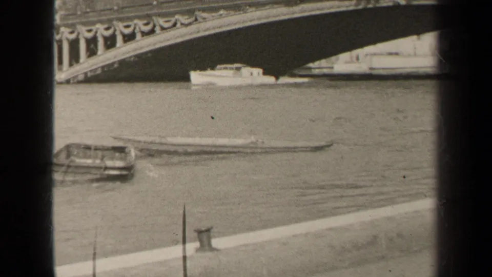 1947 Paris home-movie frame showing a small boat on the river near an ornate bridge and stone quay.