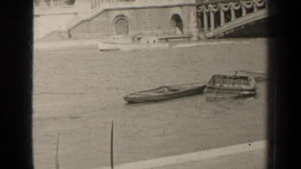 Paris home-movie frame showing a small river boat beside moored craft near a bridge and stone quay.