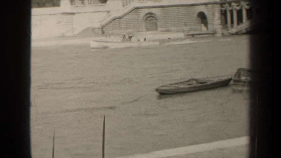 1947 Paris 8mm frame showing a small boat on river water below a stone embankment with arches, steps, and dark film borders.