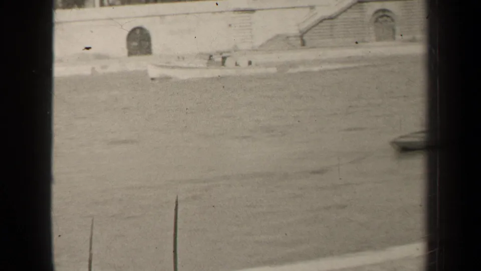 1947 Paris river view on 8mm film, with a stone embankment, arched opening, steps, and a small boat near the frame edge.