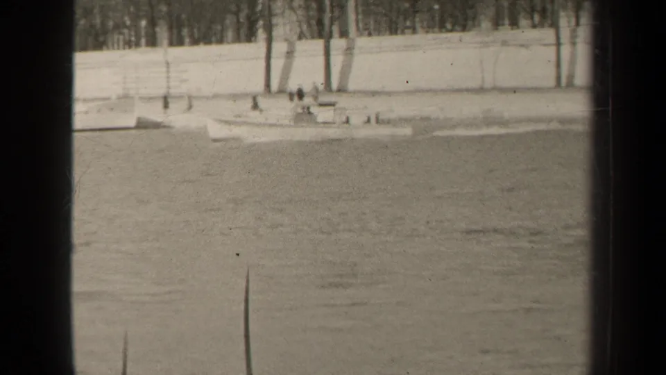 A small motorboat with indistinct people aboard or nearby travels along a Paris waterway in grainy 1947 8mm footage.