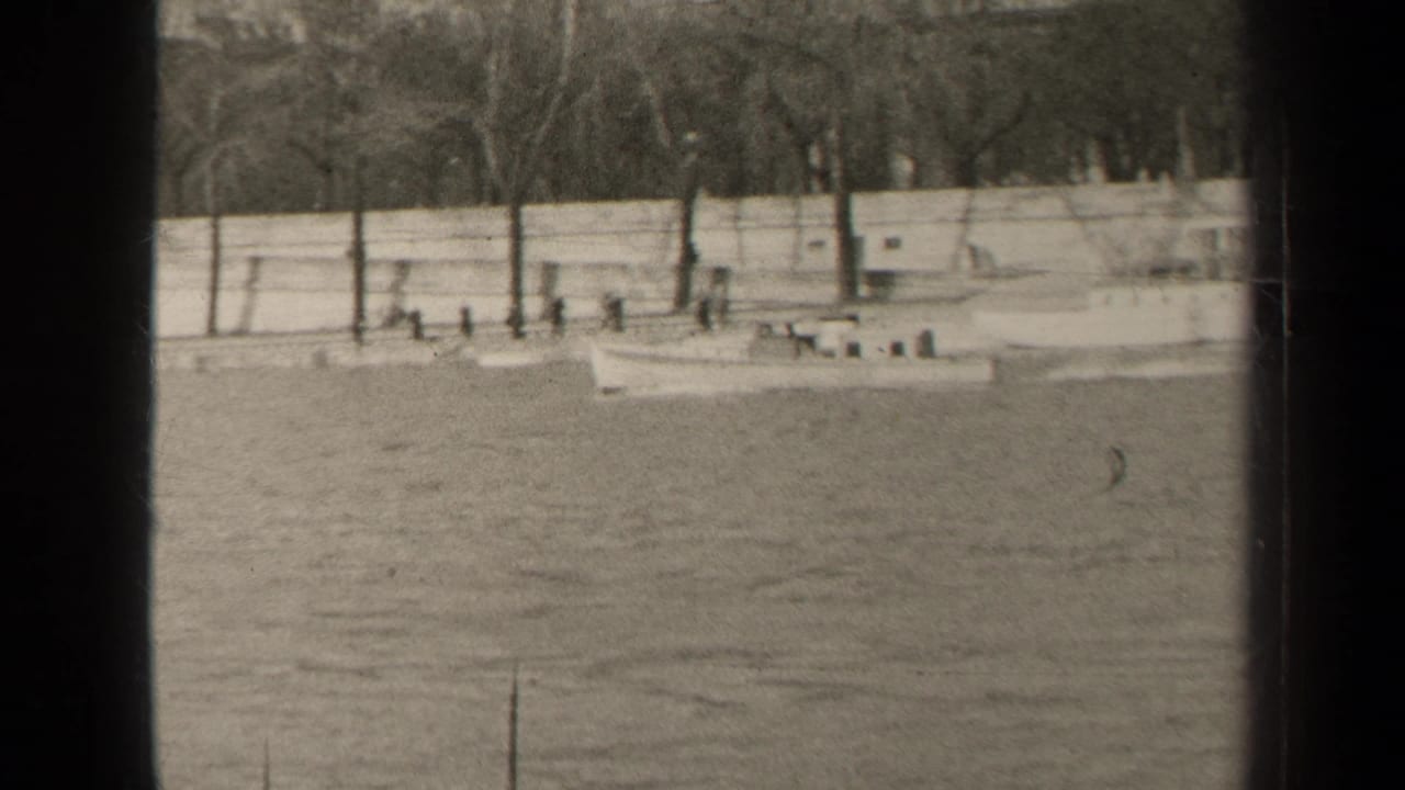 Small boat on water beside a stone embankment with trees and pedestrians.